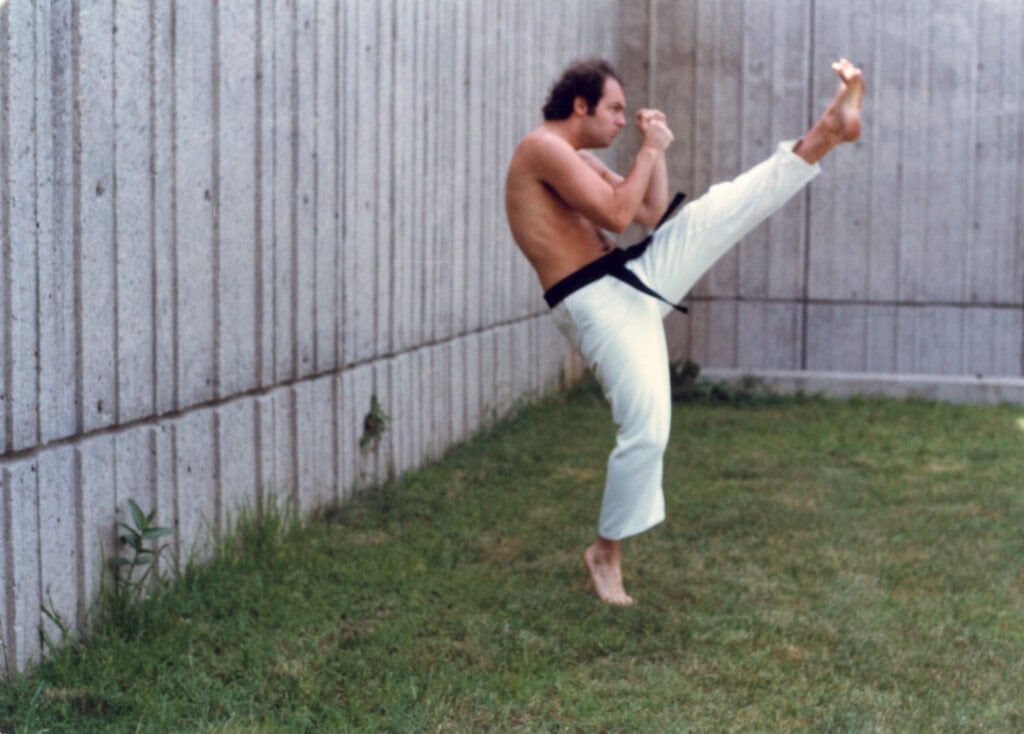 Ray Swanson executing a high kick outdoors in a karate gi and black belt, circa 1980