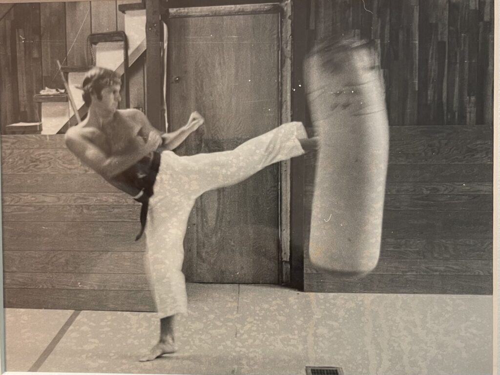 Ray Swanson practicing a roundhouse kick on a heavy bag at his St. Louis karate dojo, circa 1979