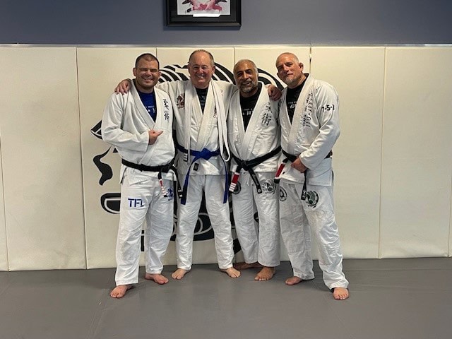 Ray Swanson receiving his BJJ blue belt, standing with his three black belt coaches at his Brazilian jiu-jitsu gym, 2024